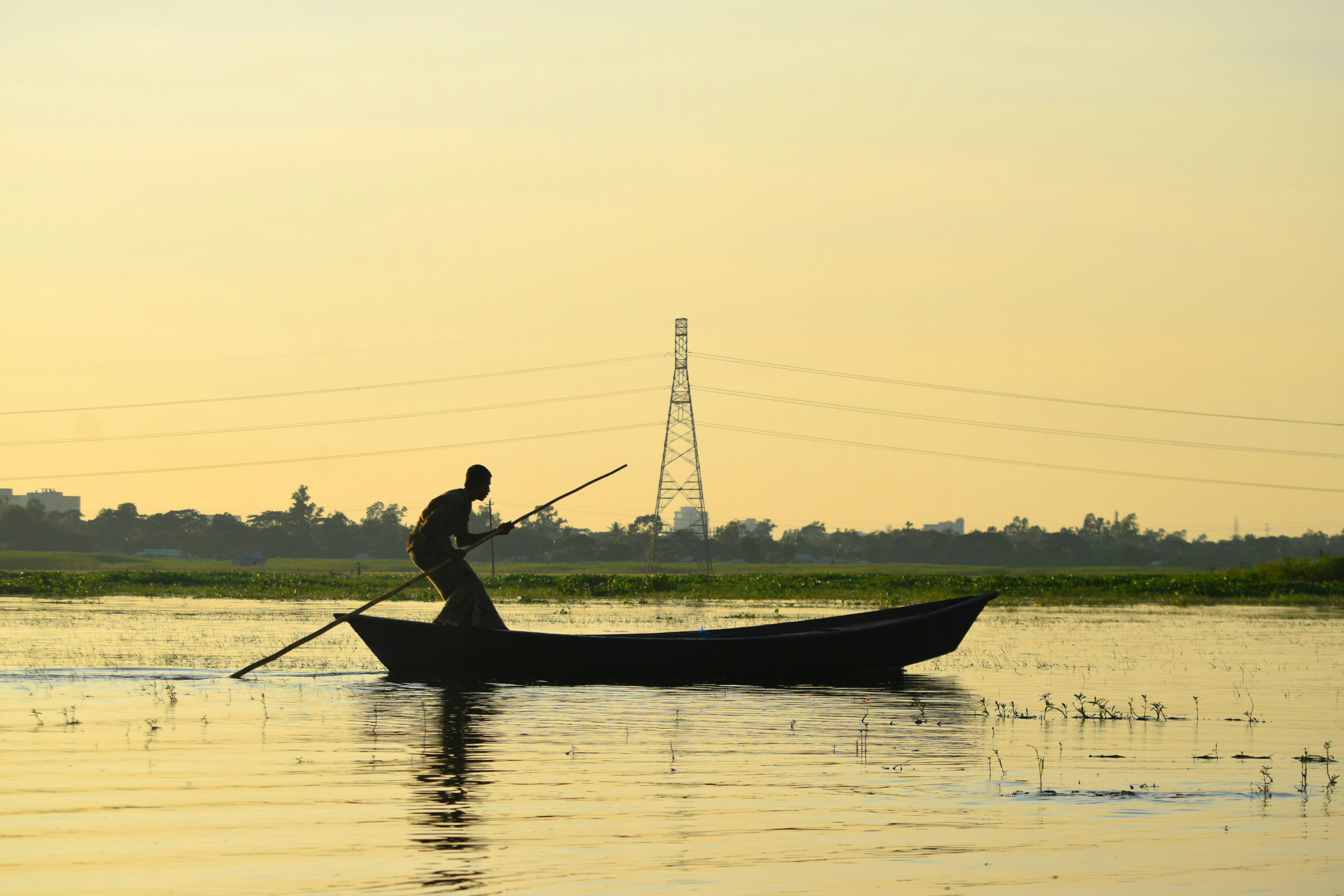 A fisherman rows a boat on a still river at golden hour in Bangladesh